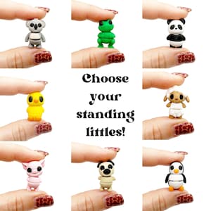 May include: A collection of small, standing animal figurines, including a koala, frog, panda, chick, sheep, pig, pug, and penguin. The text "Choose your standing littles!" is displayed in the center.