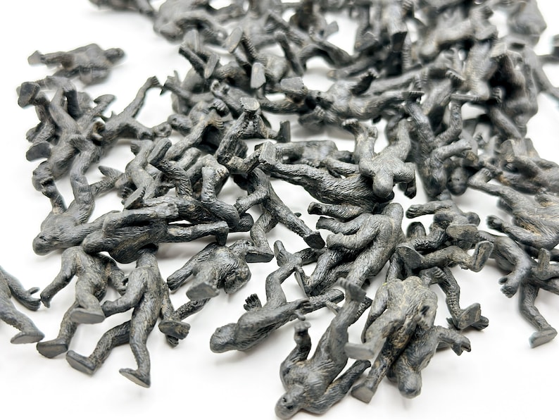 May include: A large group of small, gray plastic toy figures of Bigfoot or Sasquatch. The figures are scattered on a white surface.