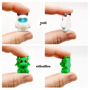 May include: Miniature figurines of a yeti and a Cthulhu. The yeti is white with blue accents and small horns. The Cthulhu is green with orange eyes and wing-like features. The word "yeti" and "cthulhu" are printed on the image.