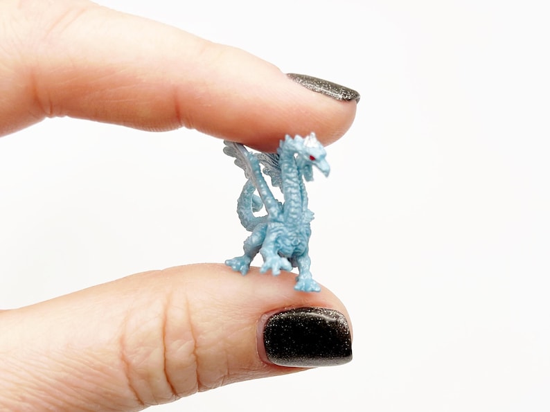 Peut inclure: Une petite figurine de dragon en plastique bleu clair avec des yeux rouges. Le dragon a des ailes et une longue queue.