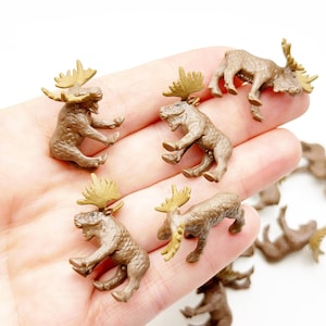 Könnte beinhalten: Eine Sammlung kleiner, brauner Elchfiguren mit detaillierten Geweihen. Die Elche befinden sich in verschiedenen Posen, einige stehen und andere sitzen. Die Figuren bestehen aus einem festen Material und werden wahrscheinlich für Bastelarbeiten oder Dekoration verwendet.
