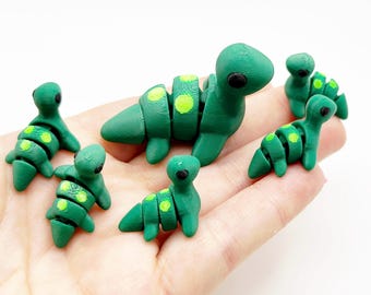 May include: A collection of green, segmented, toy-like creatures with yellow-green spots. The creatures have a rounded head and a segmented body. The toys are arranged on a light background.