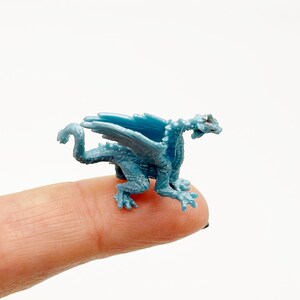 Peut inclure: Une petite figurine de dragon en plastique bleu avec des ailes, perch&eacute;e sur un doigt.
