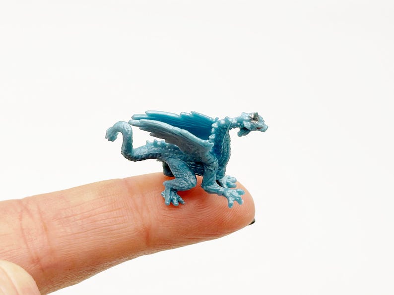 Peut inclure: Une petite figurine de dragon en plastique bleu avec des ailes, perch&eacute;e sur un doigt.
