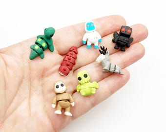 May include: A collection of seven small, articulated plastic figurines including a green turtle, a red segmented worm, a white yeti, a black owl, a grey deer, a tan creature, and a light green tentacled figure, all resting on an open palm.