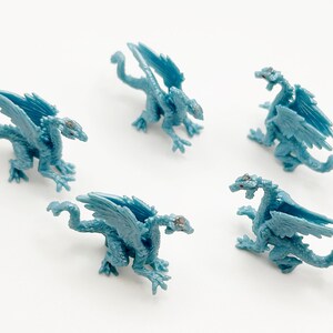 Peut inclure: Cinq figurines de dragon en plastique bleu avec des ailes et des queues. Les dragons sont pos&eacute;s dans diff&eacute;rentes positions, certains avec les ailes d&eacute;ploy&eacute;es et d'autres avec les ailes repli&eacute;es.