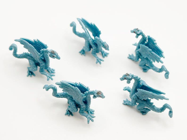 Peut inclure: Cinq figurines de dragon en plastique bleu avec des ailes et des queues. Les dragons sont pos&eacute;s dans diff&eacute;rentes positions, certains avec les ailes d&eacute;ploy&eacute;es et d'autres avec les ailes repli&eacute;es.