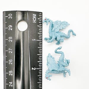 Peut inclure: Deux petites figurines de dragon en plastique bleu avec des yeux rouges. Les dragons mesurent environ 5 cm de long et sont pos&eacute;s avec leurs ailes d&eacute;ploy&eacute;es.