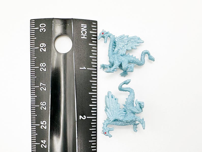 Peut inclure: Deux petites figurines de dragon en plastique bleu avec des yeux rouges. Les dragons mesurent environ 5 cm de long et sont pos&eacute;s avec leurs ailes d&eacute;ploy&eacute;es.