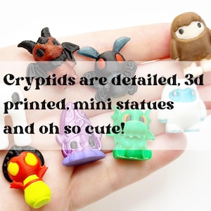 May include: A collection of colorful, 3D-printed mini cryptid statues. The text in the image reads "Cryptids are detailed, 3d printed, mini statues and oh so cute!" The statues include a red and yellow creature, a purple creature, and a green dragon.