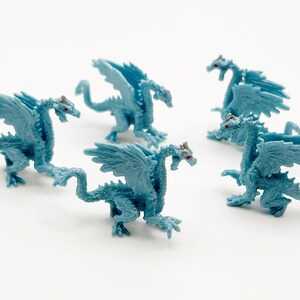 Peut inclure: Cinq dragons en plastique bleu avec des ailes. Les dragons ont deux t&ecirc;tes et sont pos&eacute;s dans diff&eacute;rentes positions.