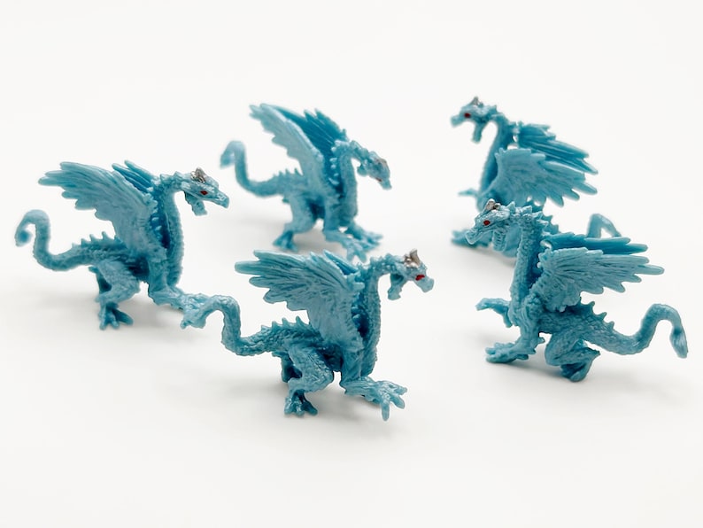 Peut inclure: Cinq dragons en plastique bleu avec des ailes. Les dragons ont deux t&ecirc;tes et sont pos&eacute;s dans diff&eacute;rentes positions.