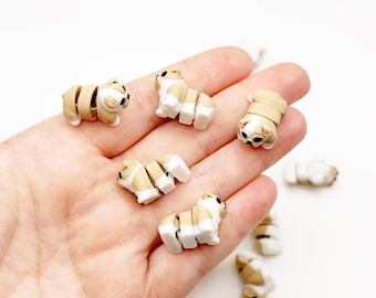 Op de afbeelding: Een verzameling kleine, gearticuleerde hondvormige beeldjes gemaakt van beige en wit materiaal. Elk beeldje heeft een gesegmenteerd lichaam met een kop, romp en achterkant die verbonden zijn voor beweging, afgewerkt met zwarte details voor ogen en neus.