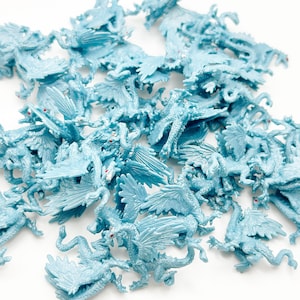 Peut inclure: Un grand groupe de figurines de dragons en plastique bleu clair. Les dragons ont des ailes, des queues et des yeux rouges.