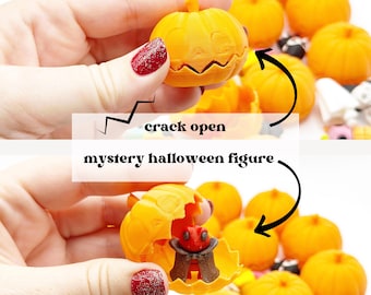 Op de afbeelding: Een verzameling kleine oranje pompoenvormige bakjes. Eén pompoen wordt opengebroken om een kleine rode Halloween-verrassingsfiguur met een bruine cape te onthullen. De tekst crack open en mystery halloween figure is zichtbaar.