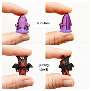 May include: Miniature purple Kraken and red Jersey Devil figurines. The Kraken has a bulbous head with a heart-shaped design and a ruffled base. The Jersey Devil has bat wings and horns. The text "kraken" and "jersey devil" are in the image.