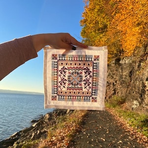 Peut inclure: Un carr&eacute; de lin blanc avec un motif brod&eacute; color&eacute; pr&eacute;sentant un motif g&eacute;om&eacute;trique avec des accents floraux. La broderie est dans des tons de rouge, orange, jaune, vert et marron.