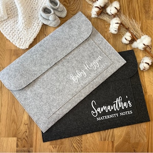 May include: Two felt folders, one grey and one black, with white text. The grey folder says "Baby Higgins Pregnancy Notes" and the black folder says "Samantha's Maternity Notes".