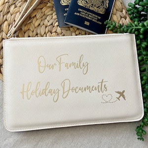 May include: A cream-coloured zippered pouch with a gold inscription that reads "Our Family Holiday Documents" and a gold airplane with a heart trailing behind it.