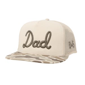 May include: A beige and tan baseball cap with the word "Dad" embroidered in a script font. The brim features a camouflage pattern, and the back has a mesh design. A logo is on the side.