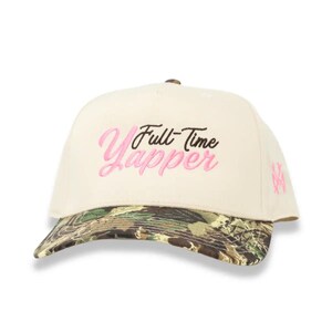 May include: A cream-colored baseball cap featuring the embroidered text Full-Time Yapper in black and pink script. The brim displays a green, brown, and black camouflage pattern. A small pink embroidered logo is visible on the side panel.