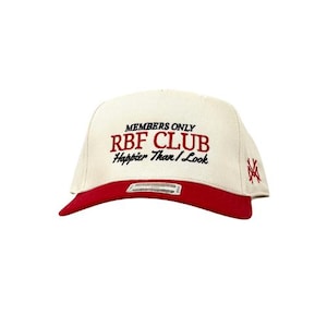 May include: A cream-colored baseball cap with a red brim. The cap features the text "MEMBERS ONLY RBF CLUB Happier Than I Look" in red and black embroidery. A stylized logo is on the side.