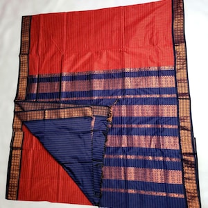 May include: A vibrant red and navy blue textile with intricate gold-colored border detailing. The fabric features a striped pattern in the navy section and a textured appearance in the red section. The textile is folded, revealing both sides.