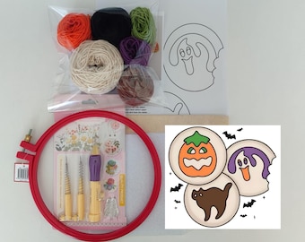 Op de afbeelding: Een punch needle borduurset met een rode plastic borduurring, een punch needle tool met een paars handvat en diverse kleine strengen garen in oranje, zwart, groen, paars, bruin en crème. Inclusief een spookpatroon en een bedrukte kaart.