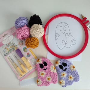 Può includere: Un kit per ago da punzonatura con un telaio da ricamo rosso, tessuto bianco e filato colorato. Il kit include tre aghi, uno schema di un fantasma con fiori e due progetti finiti di ago da punzonatura fantasma. I progetti finiti sono rosa e viola con fiori bianchi.