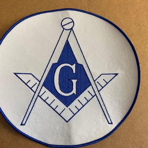 Könnte beinhalten: Runder, weißer Aufnäher mit blauem Rand, der ein blaues Freimaurersymbol zeigt. Das Symbol enthält einen Zirkel, ein Quadrat und den Buchstaben "G" in der Mitte. Der Aufnäher ist wahrscheinlich für Kleidung oder Accessoires.