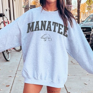 May include: A light gray sweatshirt with the word "MANATEE" printed in black across the chest. A small graphic of a manatee is printed below the word.