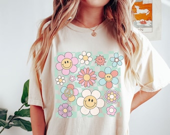 May include: A cream-colored t-shirt with a graphic print of colorful flowers and smiley faces on a checkered background.