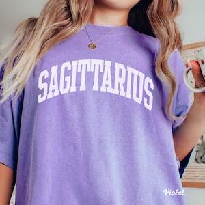 May include: A purple t-shirt with the word "SAGITTARIUS" printed in white on the front.