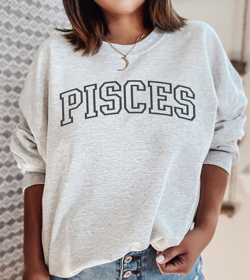 Pode incluir: Camisola de moletom cinza com a palavra "PISCES" impressa em letras pretas com contorno.