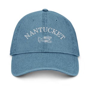 May include: A blue denim baseball cap with white embroidery that reads "NANTUCKET" with a white embroidered lobster design.