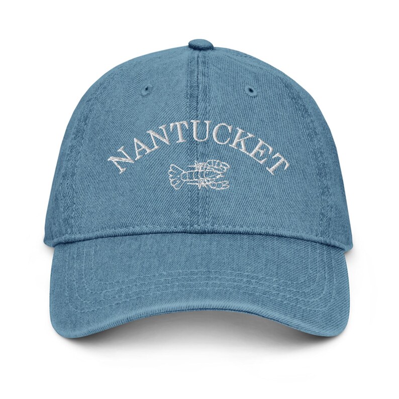 May include: A blue denim baseball cap with white embroidery that reads "NANTUCKET" with a white embroidered lobster design.