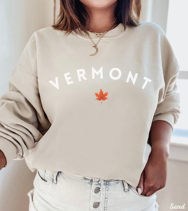 May include: A beige sweatshirt with the word "VERMONT" in white lettering and a red maple leaf graphic.