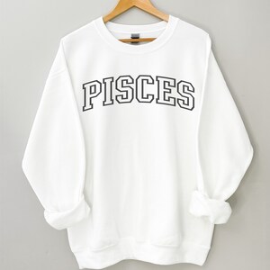 Pode incluir: Camisola branca com texto preto que diz "PISCES" em uma fonte de estilo universit&aacute;rio.