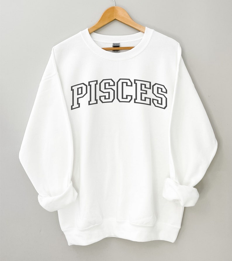 Pode incluir: Camisola branca com texto preto que diz "PISCES" em uma fonte de estilo universit&aacute;rio.