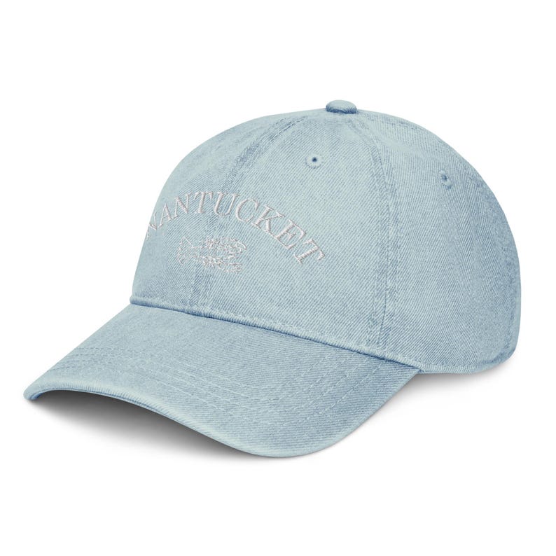 May include: A light blue denim baseball cap with white embroidered text that reads "NANTUCKET" and a small fish design.