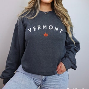 May include: Dark heather grey sweatshirt with white text that reads "VERMONT" with a red maple leaf underneath.