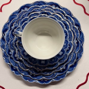 May include: A set of four blue and gold porcelain plates with a scalloped edge and intricate floral designs. The plates are stacked on top of each other, with a white porcelain teacup in the center.