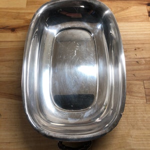 May include: A silver serving dish with two handles. The dish is oval shaped and has a raised rim.