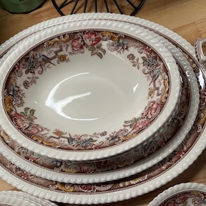 May include: A set of four white ceramic bowls with a brown and pink floral pattern. The bowls are nested inside each other, with the largest bowl on the bottom and the smallest bowl on top.