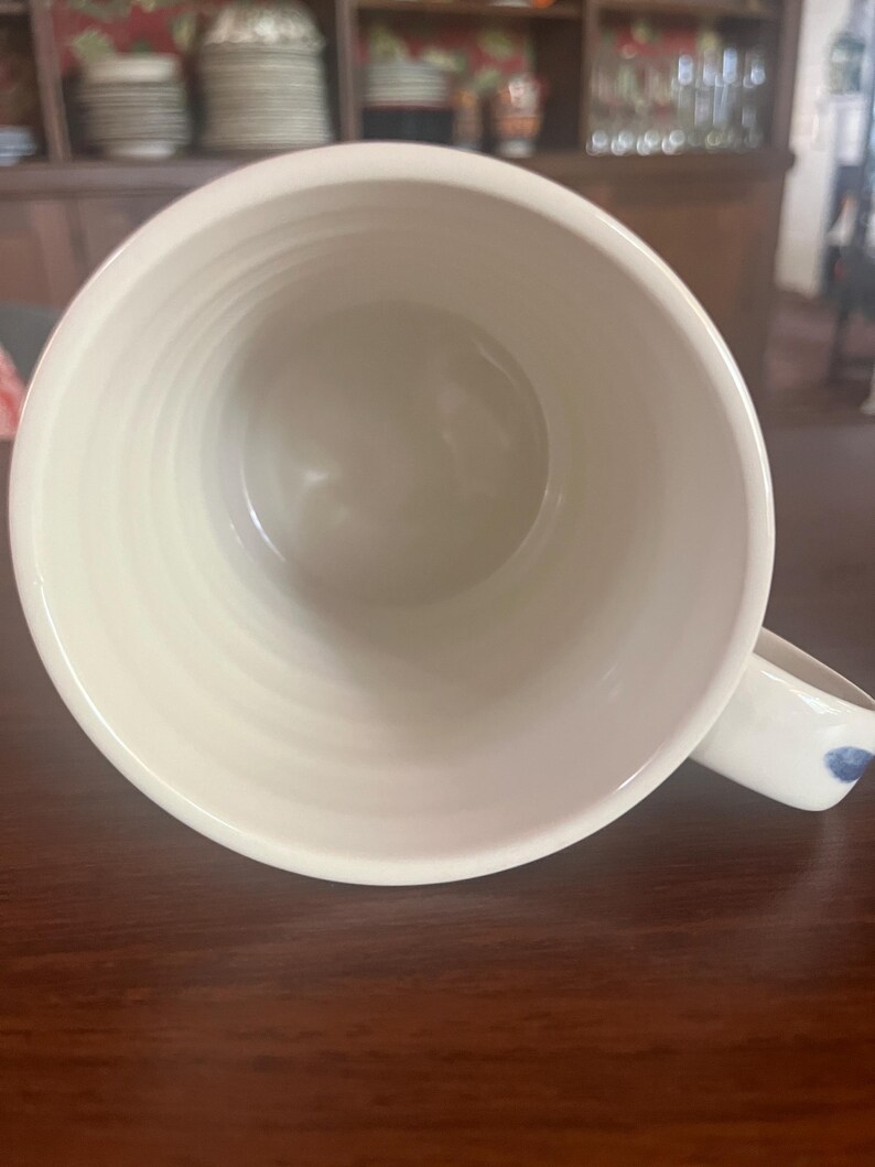 K&ouml;nnte beinhalten: Cremefarbene Keramiktasse mit breiter &Ouml;ffnung und Henkel. Der Innenraum ist glatt, hellbeige, w&auml;hrend die Au&szlig;enseite ein strukturiertes, geriffeltes Design aufweist. Der Henkel hat ein blaues Blumenmuster. Ideal f&uuml;r Tee oder Kaffee.