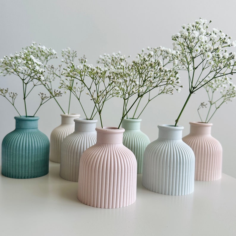 May include: A set of six small, decorative vases in various pastel colors, each with a ribbed texture. The vases are filled with white baby's breath flowers.
