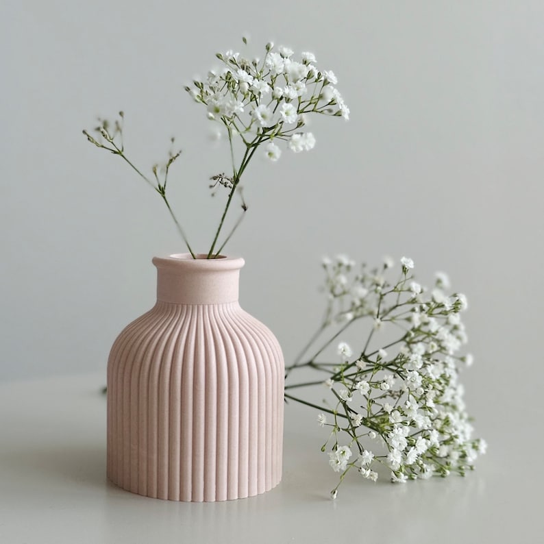 May include: A pink ceramic vase with vertical ridges, holding a bouquet of white baby's breath flowers.