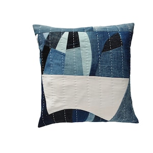 Può includere: Un cuscino blu e bianco in patchwork con un design geometrico. Il cuscino è realizzato in tessuto denim e ha un retro in cotone bianco.