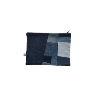 May include: A rectangular denim patchwork pouch with a brown zipper. The pouch is made from various shades of blue denim, creating a geometric pattern. A small fabric tag is attached to the side. The pouch is designed for carrying small items.