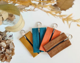 May include: Four zippered pouches with key rings. The pouches are made of different fabrics in mustard yellow, teal blue, orange, and brown corduroy.